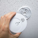 Person cleaning a smoke detector on the wall