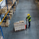 High-angle view of man worker with pallet truck working indoors in warehouse that prioritizes fire safety