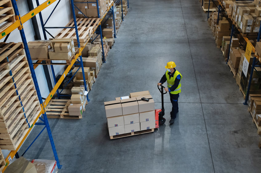 High-angle view of man worker with pallet truck working indoors in warehouse that prioritizes fire safety