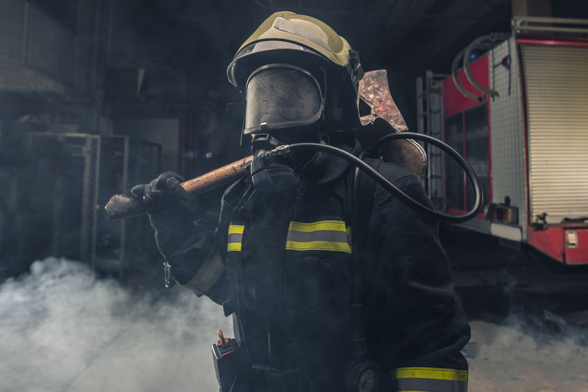 Portrait of a fireman wearing firefighter turnouts holding a rescue axe before he fights commercial fire.