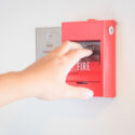 A hand is pulling a commercial fire alarm on the wall